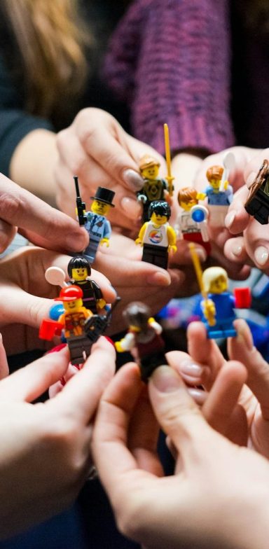 Hände halten eine Gruppe von bunten LEGO-Figuren um einen Tisch.